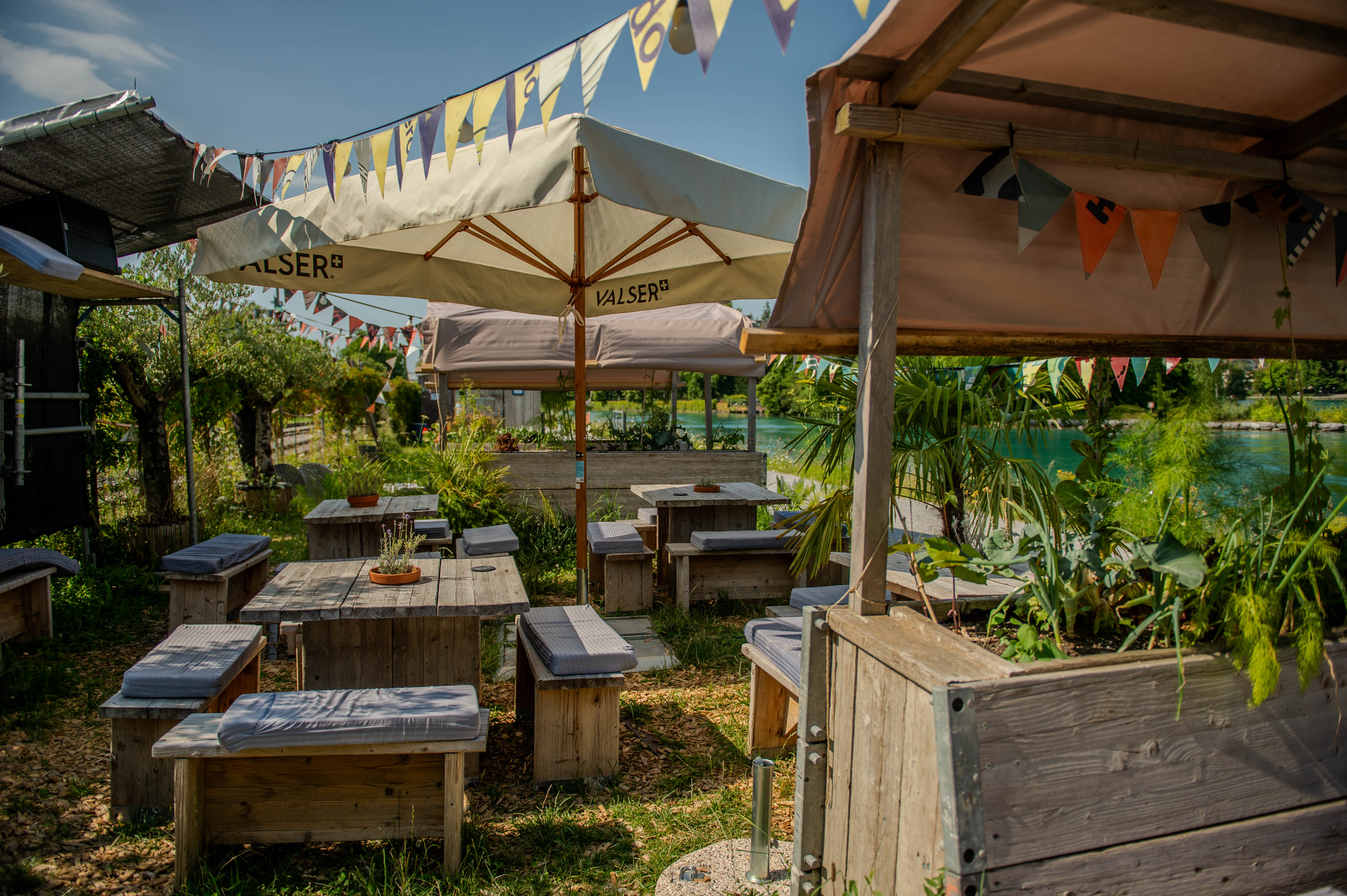 Unsere schönen Holztische und Bänke im Pop Up Thun, umgeben von üppigen Pflanzen in einem charmanten Außenbereich